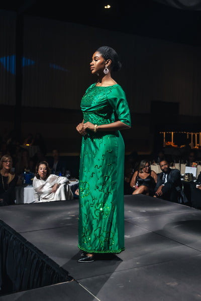 Woman in a green dress standing on a stage with an audience in the background