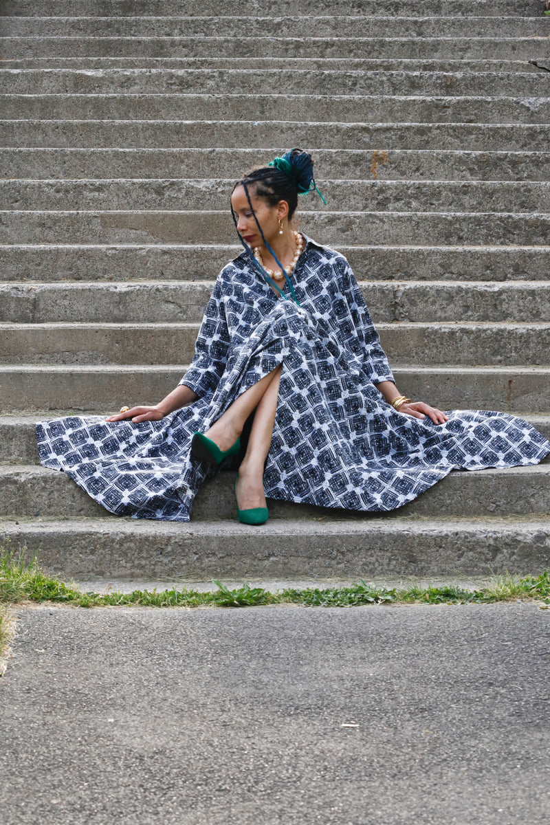 Woman sitting on steps wearing a patterned dress and green shoes.