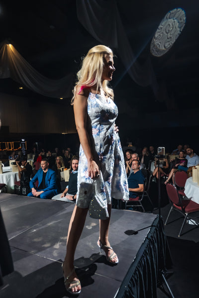 Woman in a floral dress walking on a stage with an audience in the background