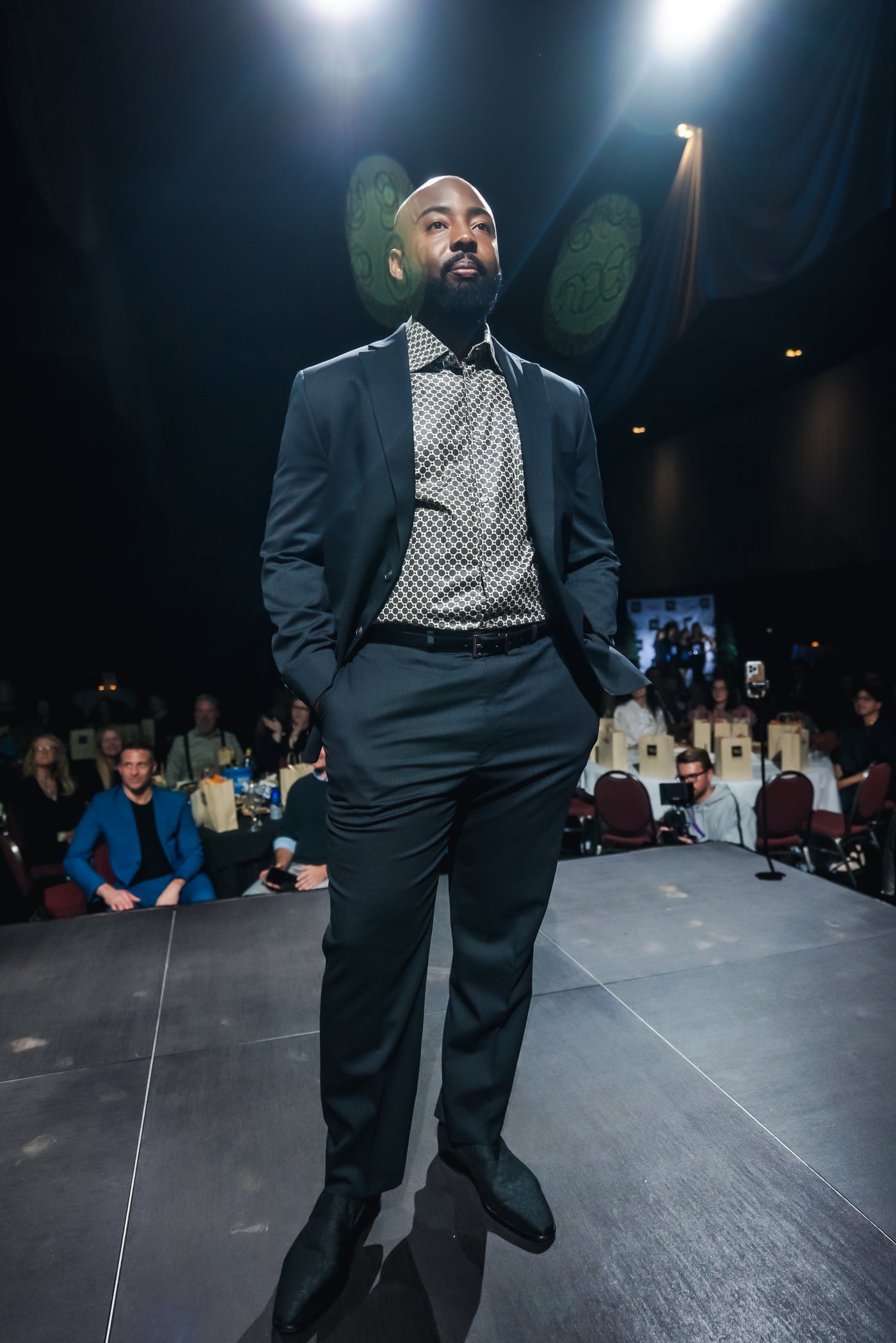 Man in a suit standing on a runway with audience and judges in the background