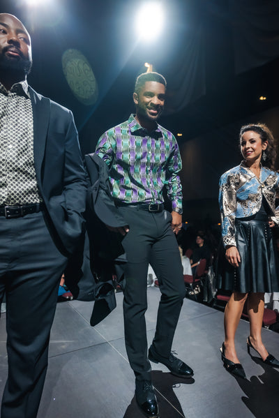 Three people walking on a runway at a fashion show.