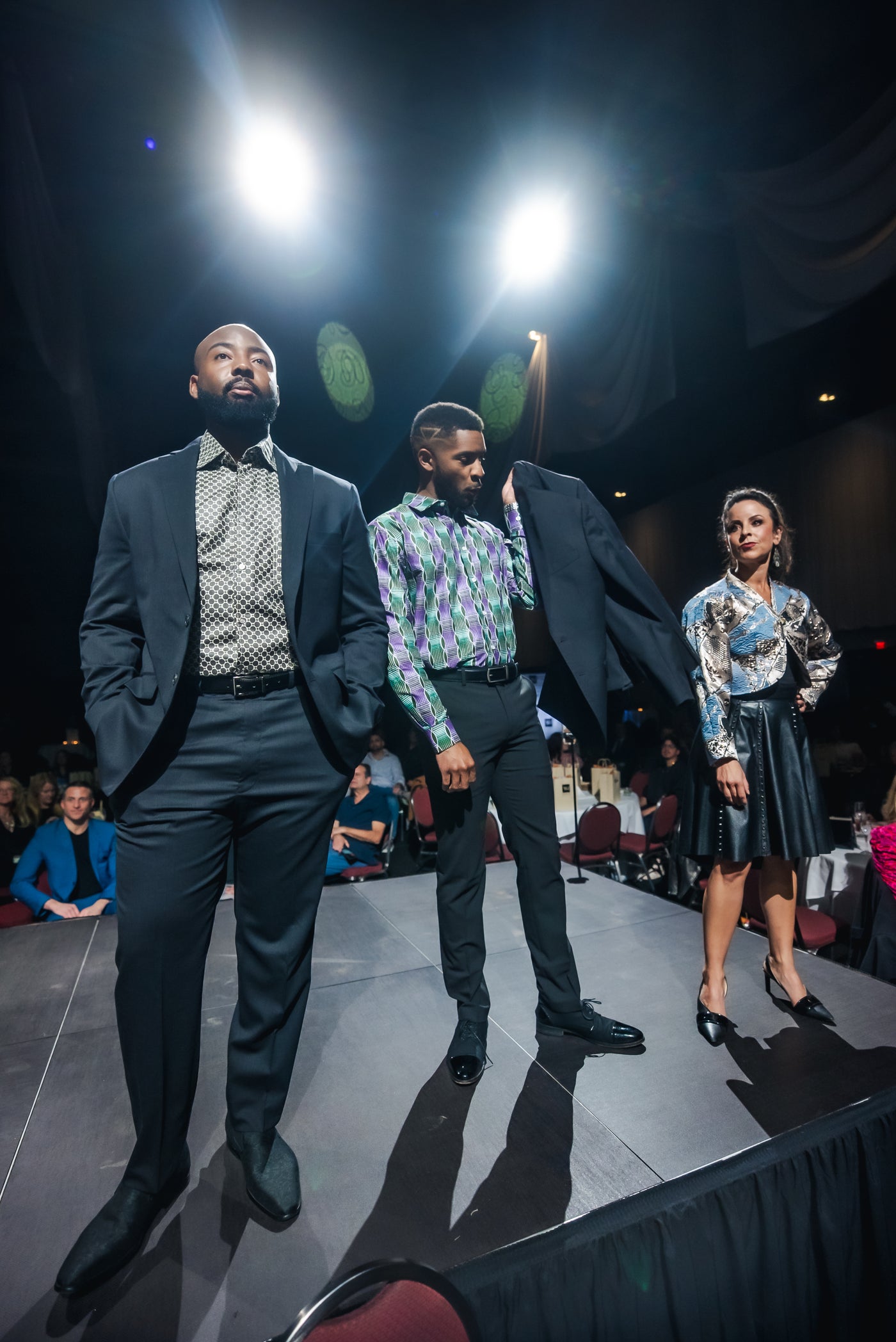 Three models on a fashion show runway with bright lights above.