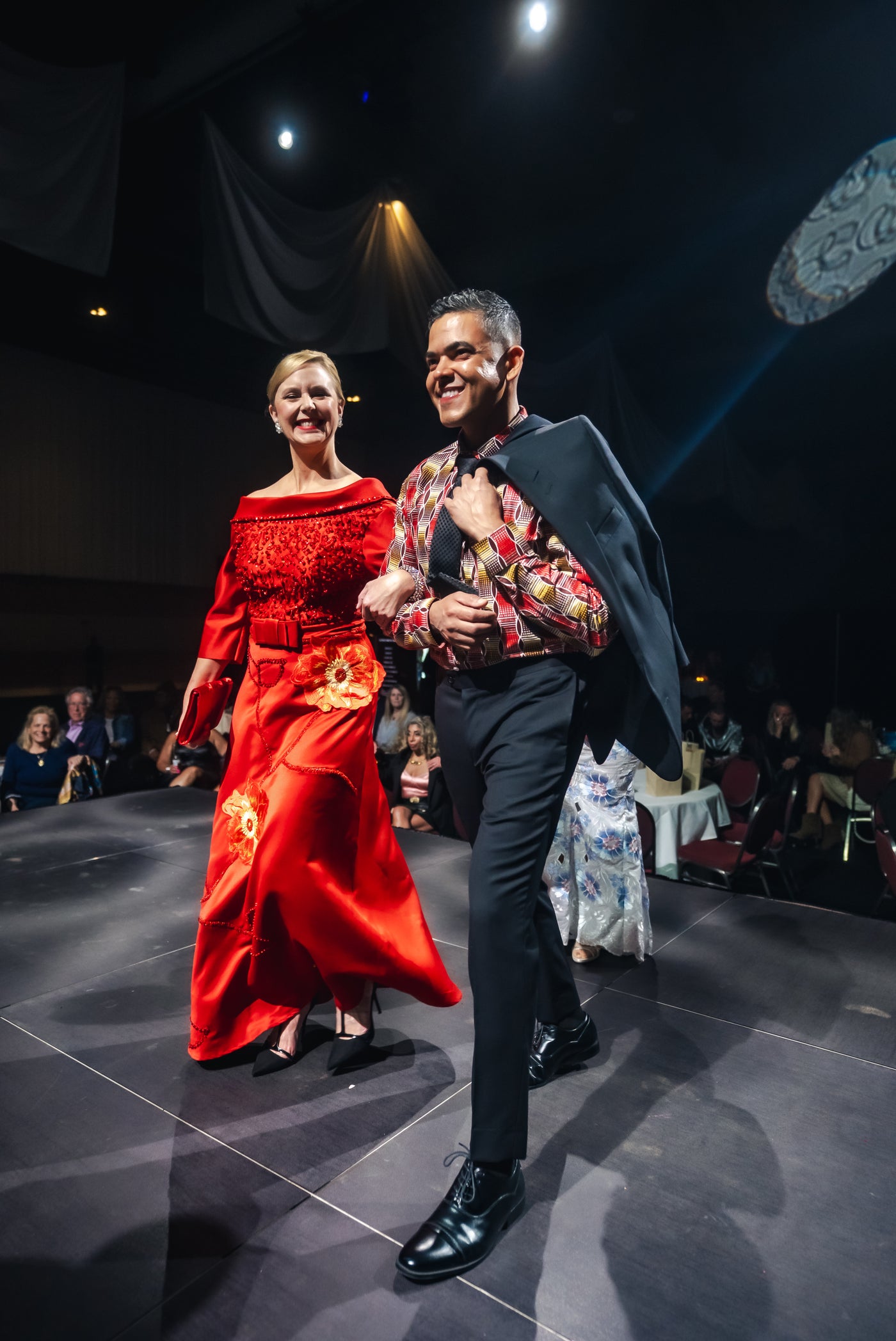 Two models on a runway, one in a red dress and the other in formal attire.