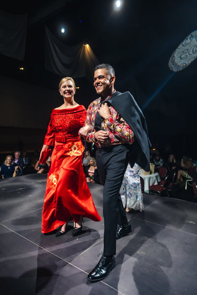 Two models on a runway, one in a red dress and the other in formal attire.